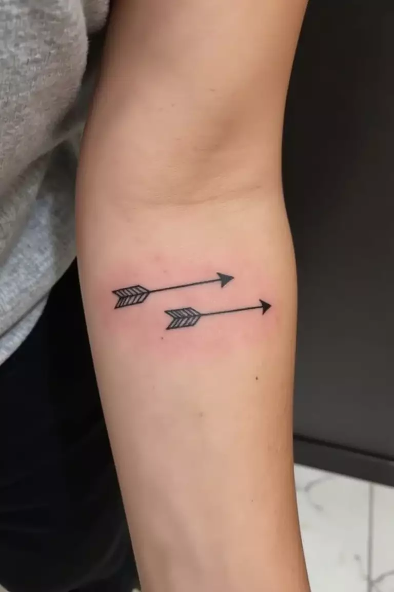 A close up shot of woman's arm with a black ink double arrow tattoo, parallel arrows pointing in opposite directions
