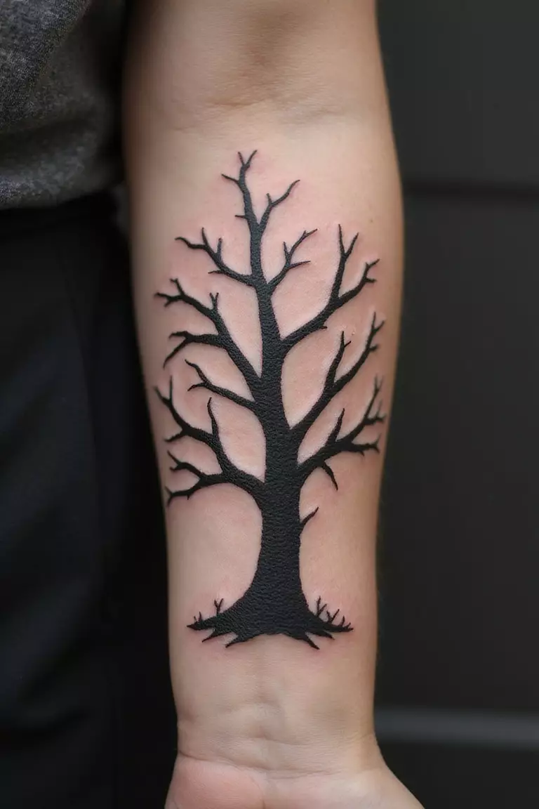 A close-up shot of a woman's arm with a black ink tattoo of a lifeless tree.