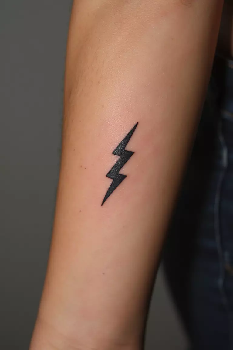 A close up shot of woman's arm with a black ink tattoo featuring a small, stylized lightning bolt symbolizing Zeus's power and authority.