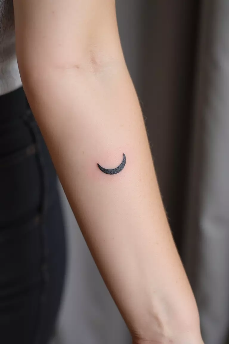A close up shot of woman's arm with a black ink tattoo of a thin crescent moon.