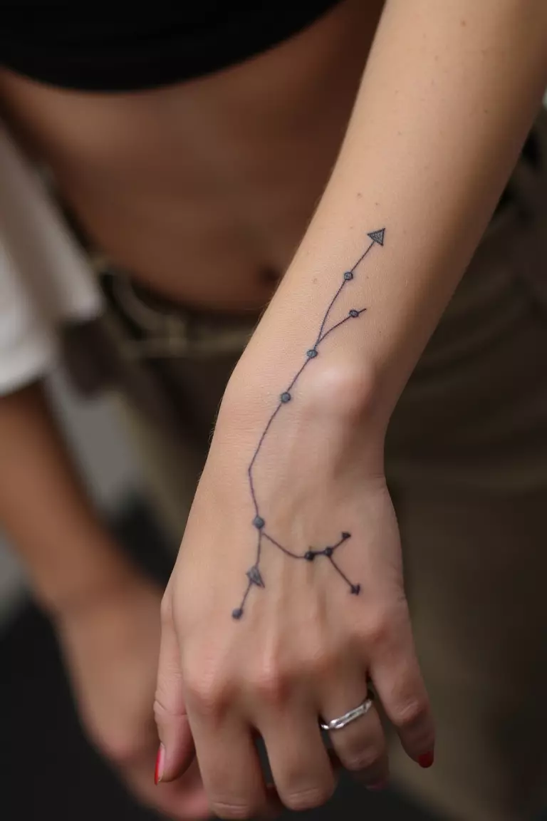 A close-up shot of a woman showing her black ink constellation tattoo design on her arm