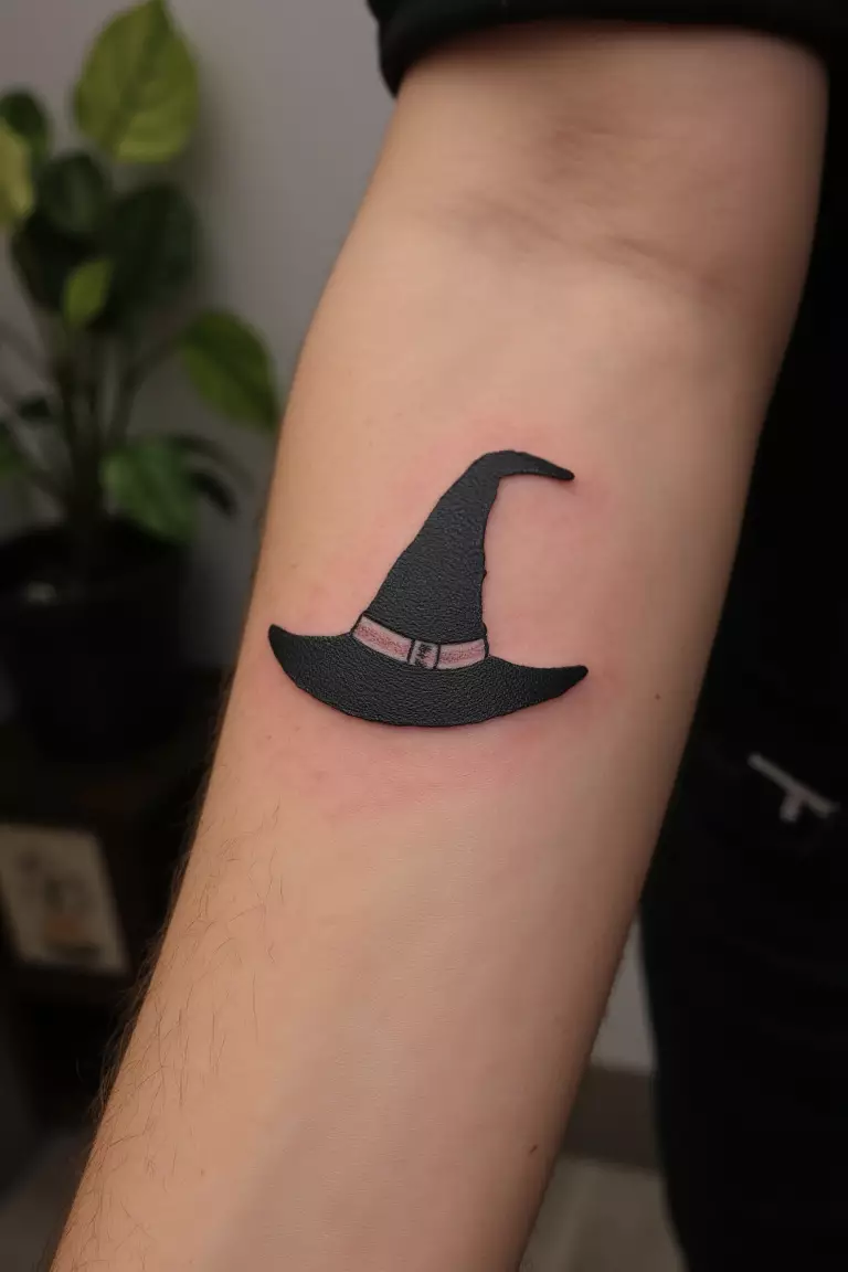 A close up shot of woman's arm with a black ink tattoo of a simple witch hat.