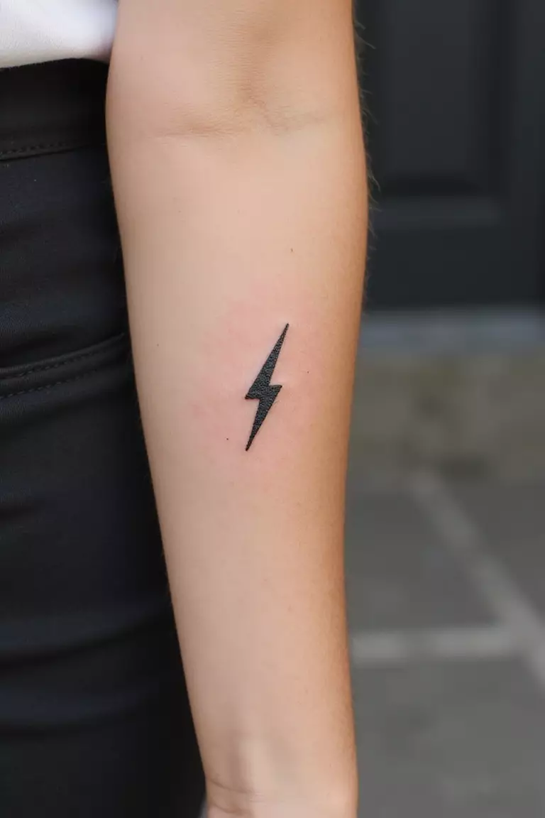 A close up shot of woman's arm with a black ink tattoo of a small, simple lightning bolt.