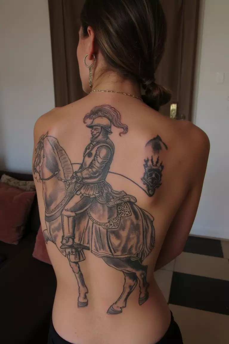 A photo of a woman with an unfinished vintage knight riding a horse tattoo, living room background.