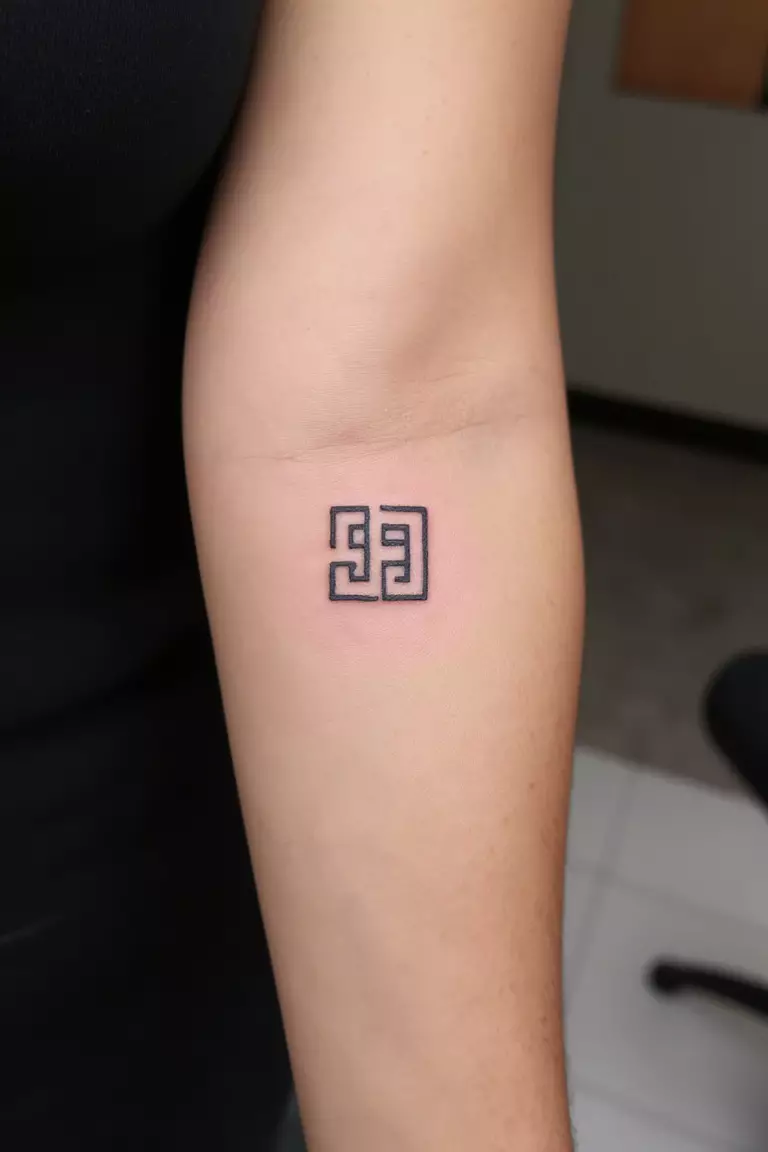 A close up shot of woman's arm with a black ink tattoo featuring a minimalist version of the classic Greek key design.
