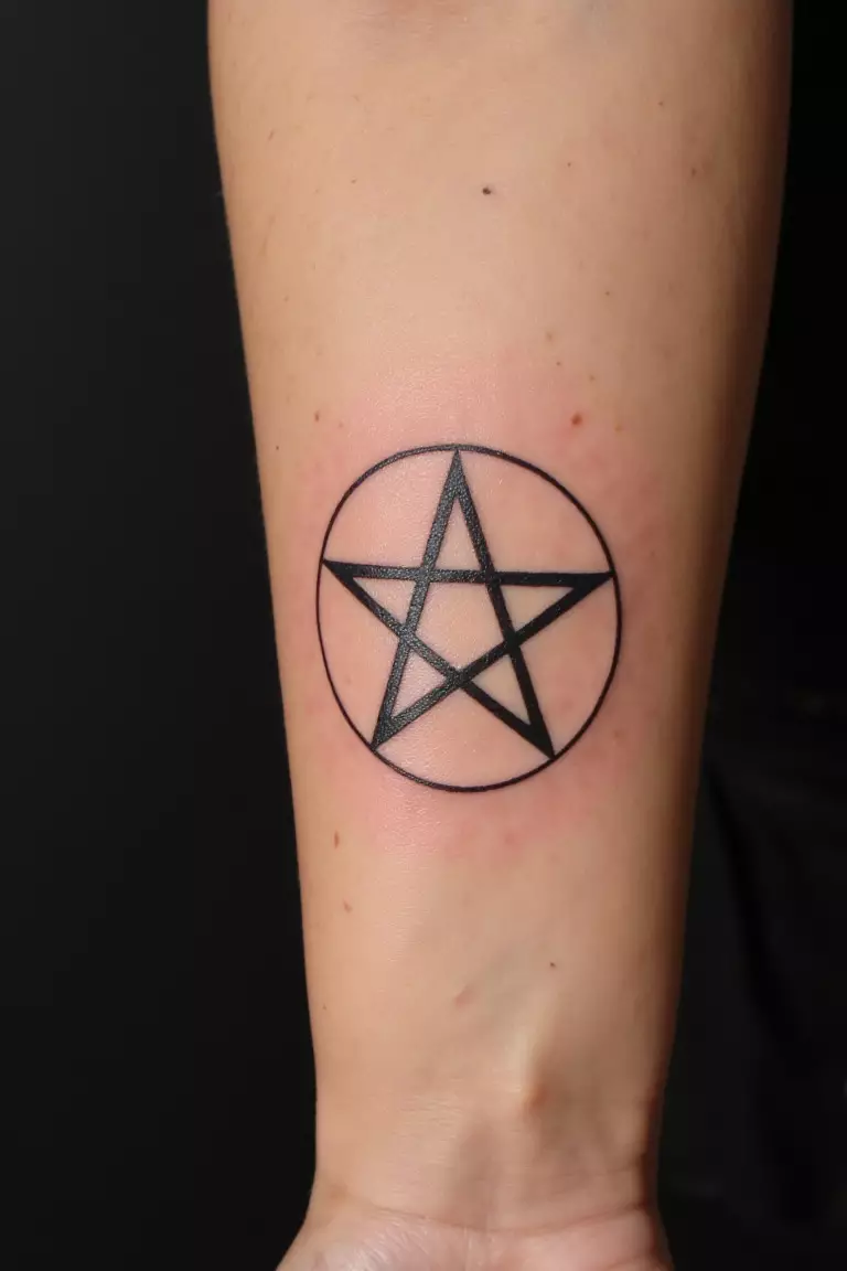 A close up shot of woman's arm with a black ink tattoo of a clean pentagram.