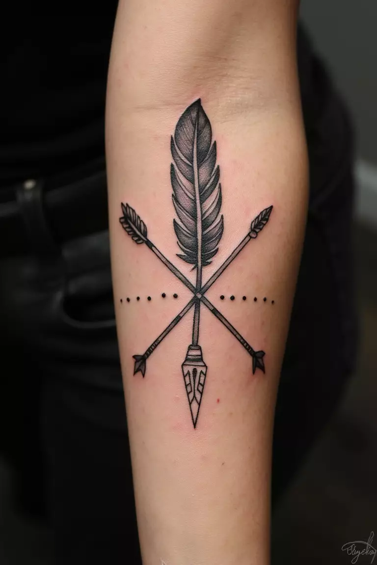 A close up shot of woman's arm with a black ink feather and arrow design tattoo, crossed elements with tribal details