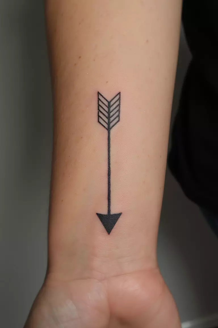 A close up shot of woman's arm with a black ink arrow pointing downward tattoo, elegant and meaningful design