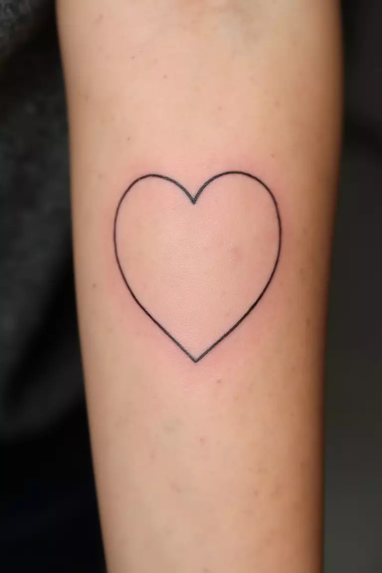 A close up shot of woman's arm with a black ink heart outline tattoo, simple clean lines