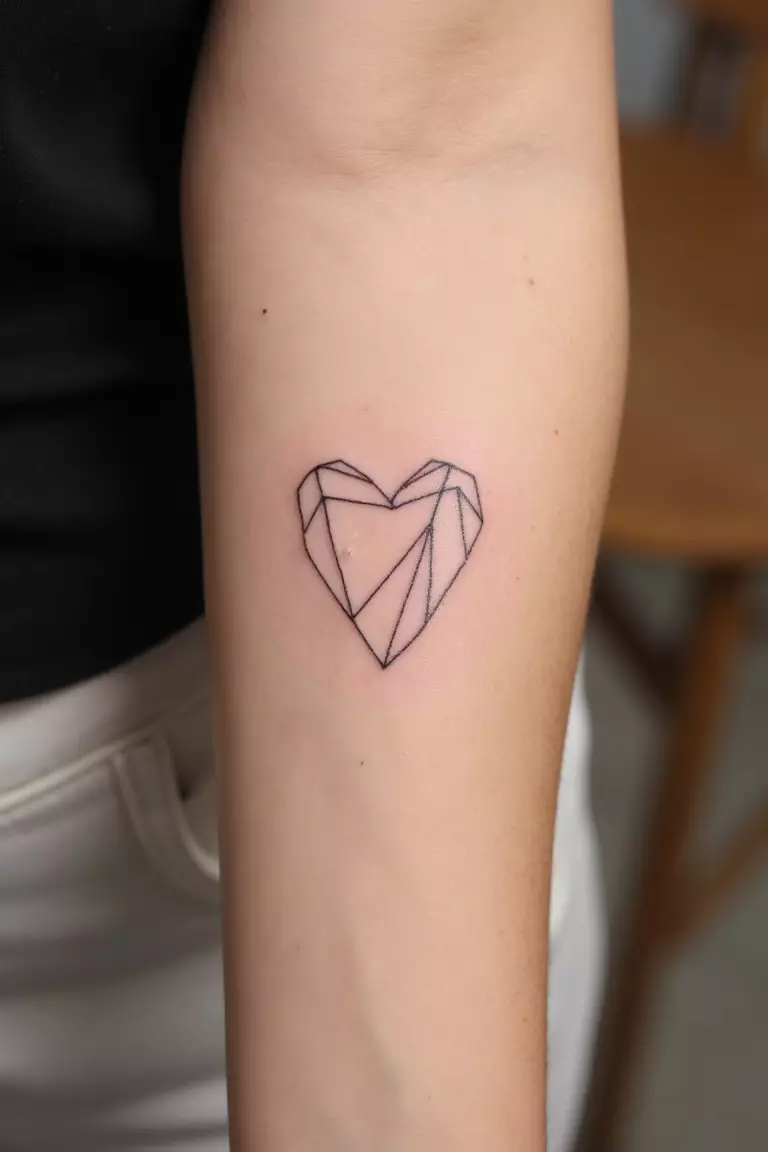 A close up shot of woman's arm with a black ink minimal geometric heart tattoo, composed of straight lines