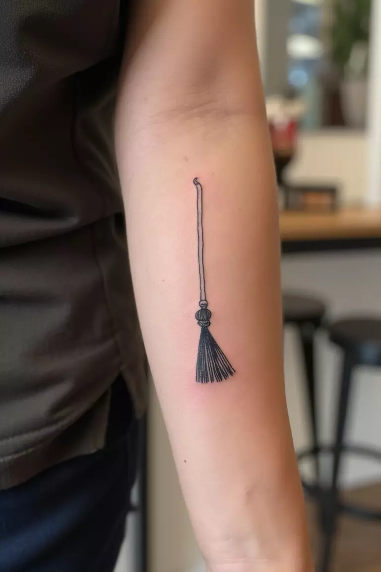 A close up shot of woman's arm with a black ink tattoo of a minimalistic broom.