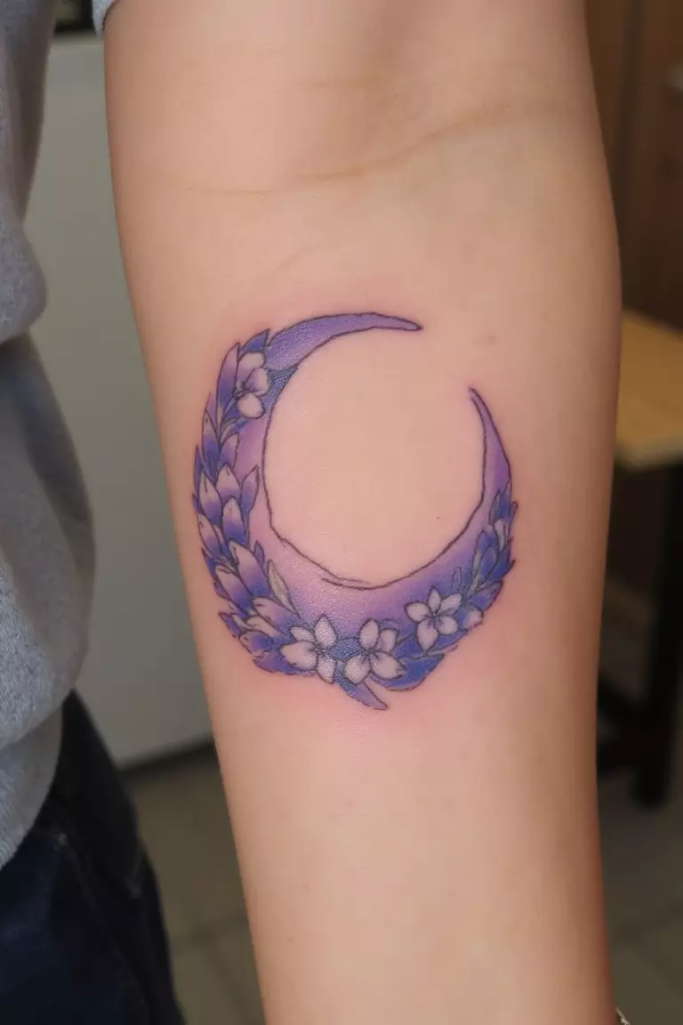 A close up shot of woman's arm with a lavender crescent moon tattoo  