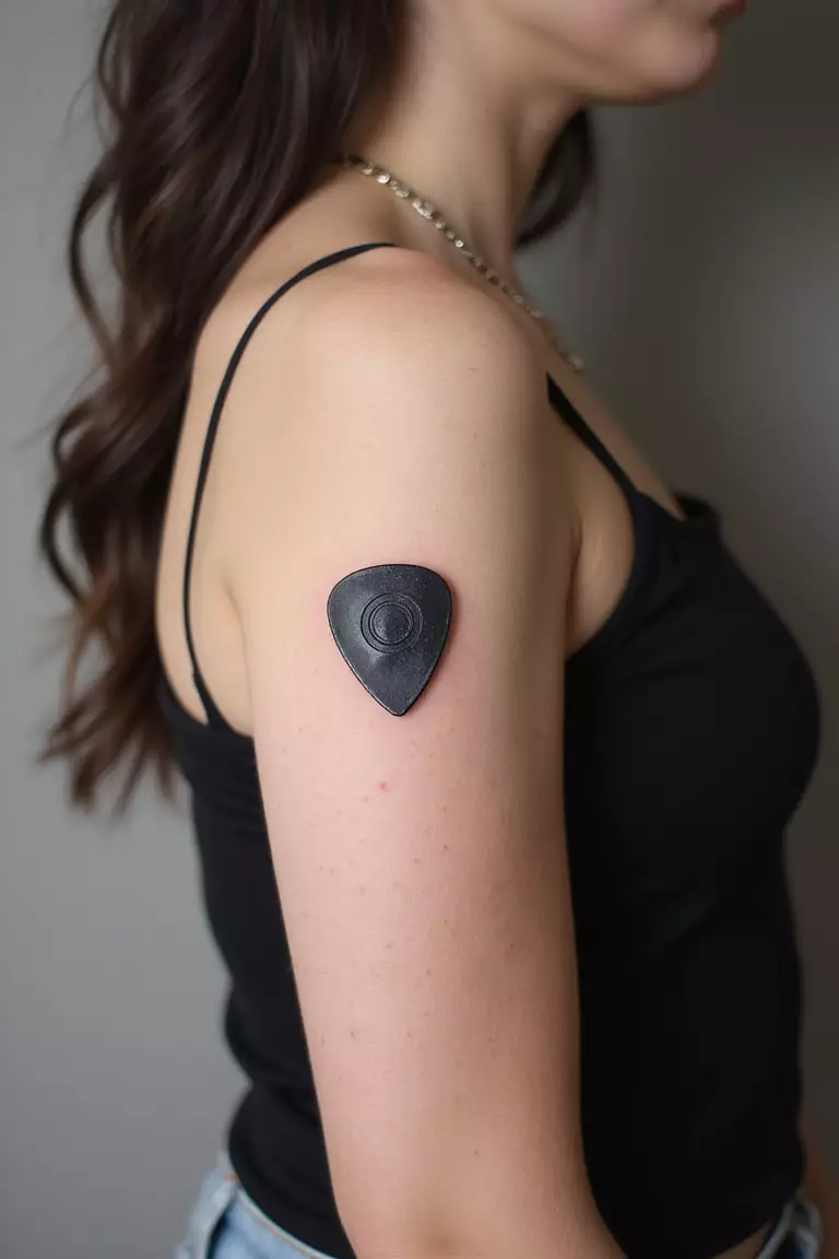 A close-up shot of a woman showing her black ink single guitar pick tattoo on her arm.
