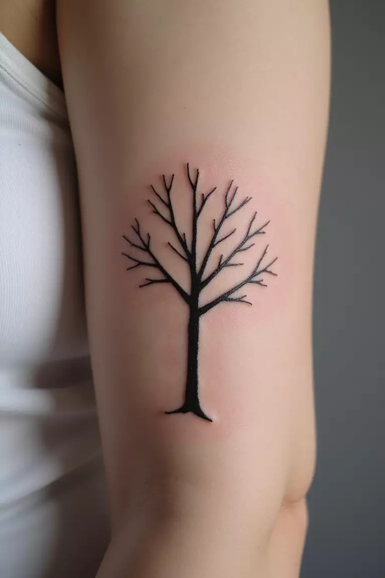 A close-up shot of a woman's arm with a black ink tattoo of a very simple, almost stick-figure-like tree.