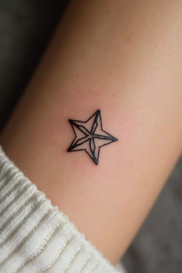 A close-up shot of a woman's arm with a black ink tattoo of a tiny, simple five-pointed star outline.