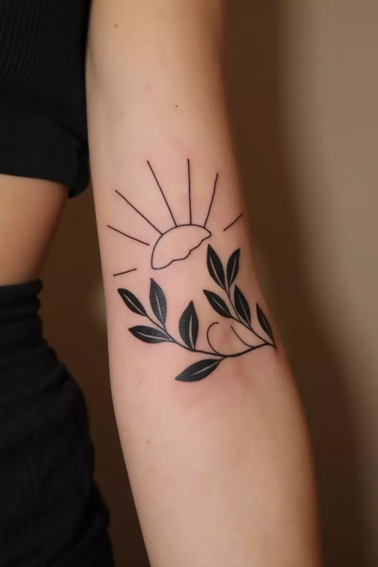 A close up shot of woman's arm with a black ink olive branch silhouette against a sun tattoo  