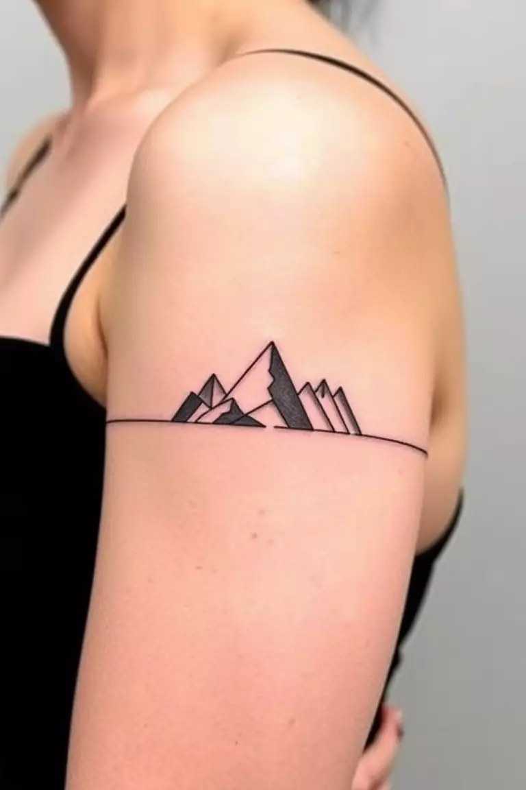 A photo of a woman with a mountain armband tattoo encircling her bicep, featuring stylized peaks and valleys.  