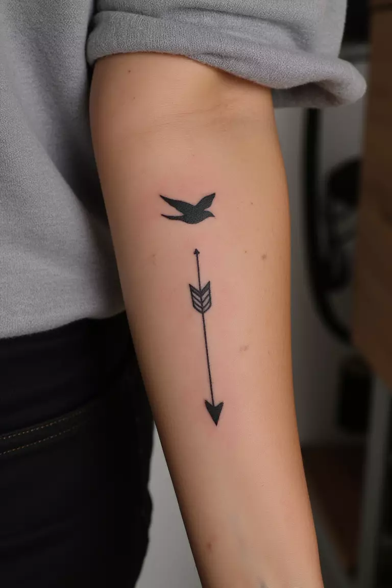 A close up shot of woman's arm with a black ink arrow and bird tattoo, bird flying near the arrow