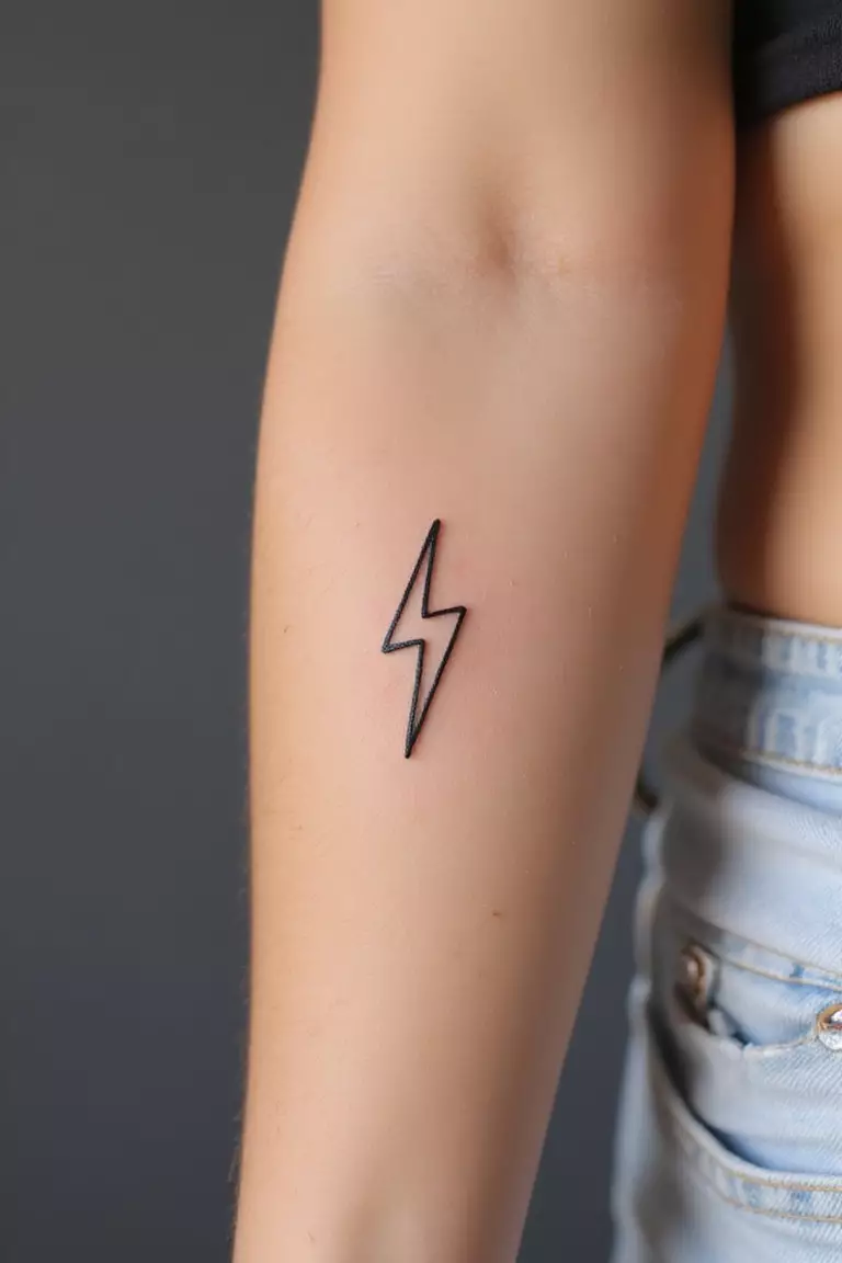 A close-up shot of a woman's arm with a black ink tattoo of a tiny, simple lightning bolt outline.