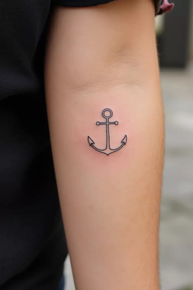 Small Anchor Outline A close up shot of woman's arm with a black ink small anchor outline tattoo.