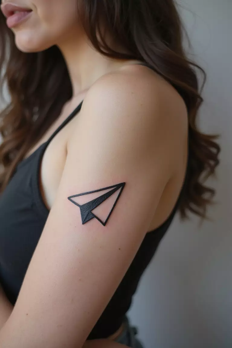 A close-up shot of a woman showing her black ink paper airplane tattoo design on her arm