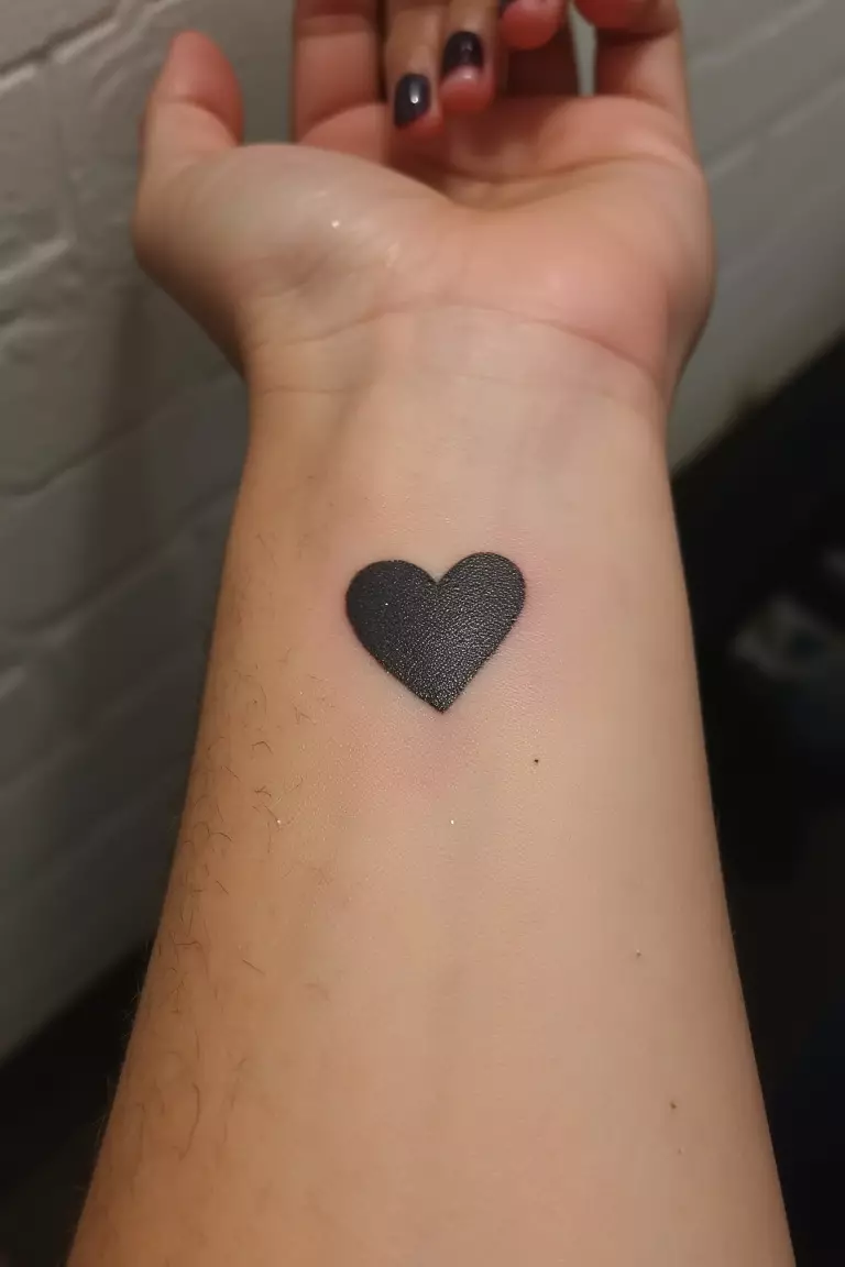 A close up shot of woman's wrist with a black ink heart tattoo, perfectly placed on pulse point