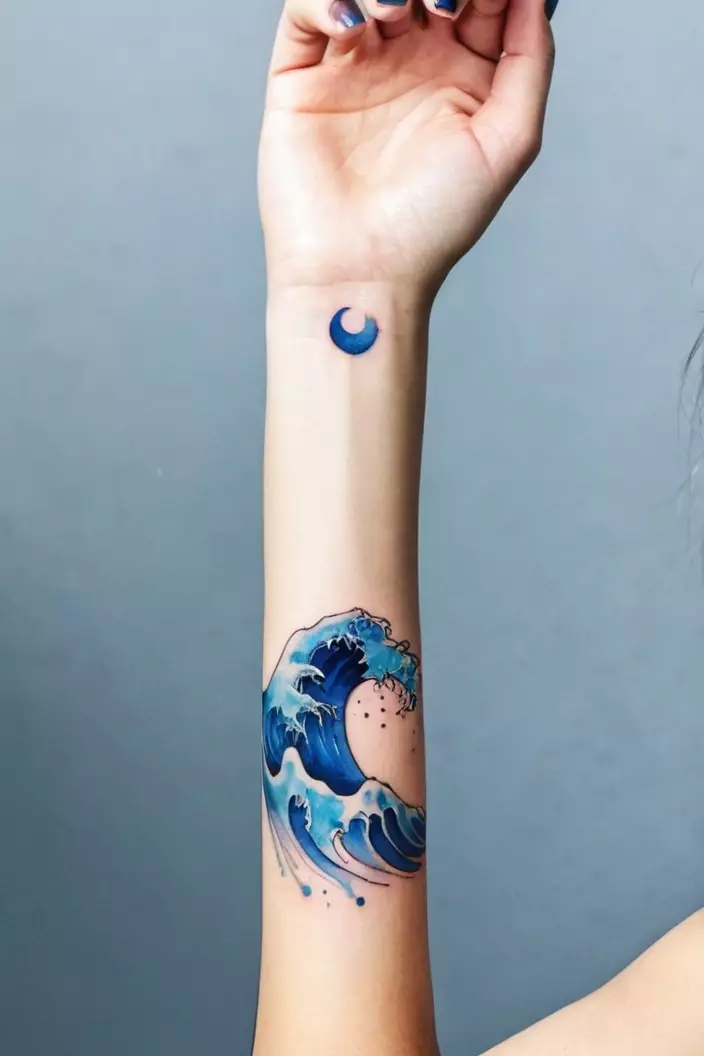 A photo of a woman displaying a blue watercolor minimal wave tattoo on her forearm.  