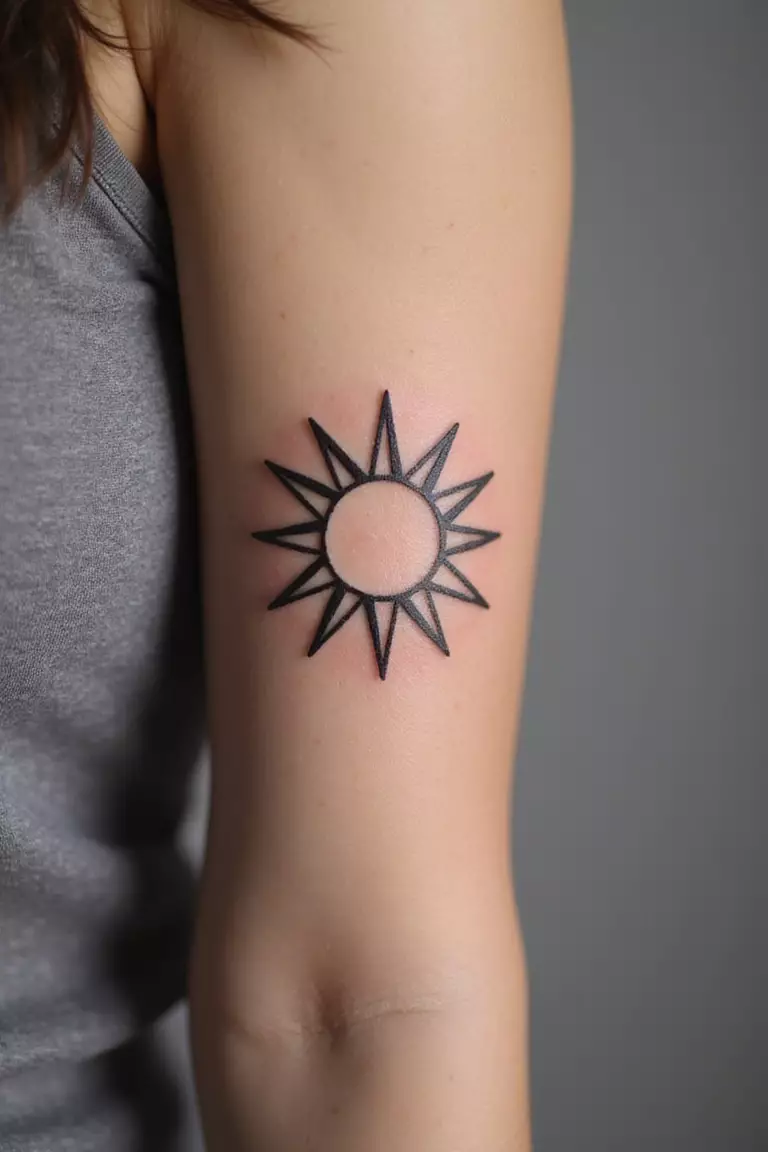 Sun A close-up shot of a woman's arm with a black ink tattoo of a minimalist sun symbol with rays.