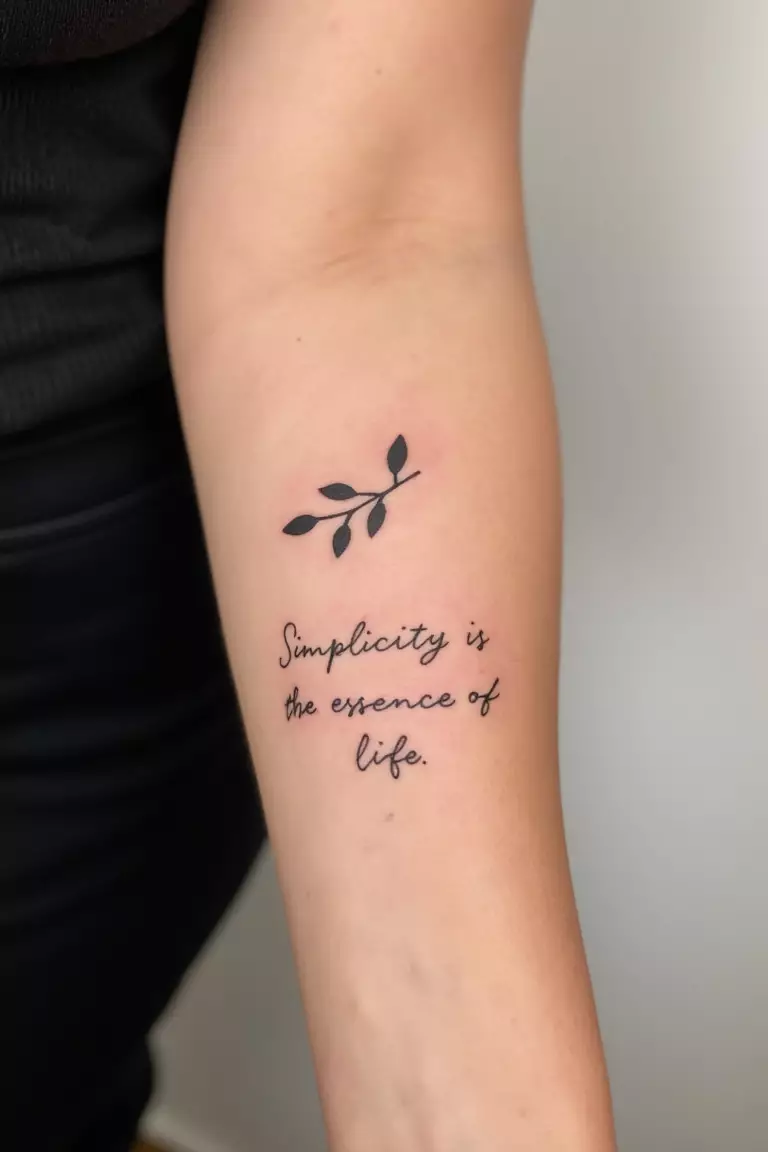 A close up shot of woman's arm with a black ink olive branch accompanied by a minimalist quote "Simplicity is the essence of life" tattoo  