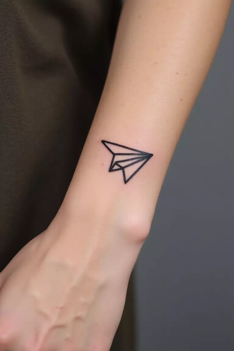 A close-up shot of a woman showing her black ink tiny paper airplane outline tattoo design on her forearm