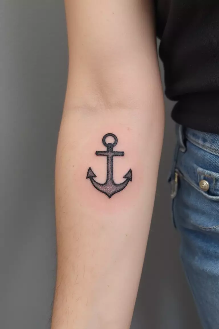 A close-up shot of a woman's arm with a black ink tattoo of a small, simple anchor outline.