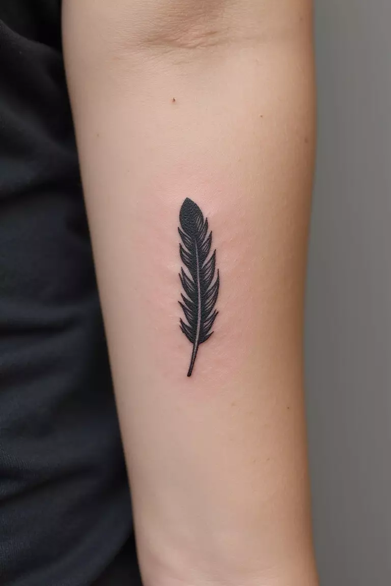 A close up shot of woman's arm with a black ink tattoo of a single, simple feather.