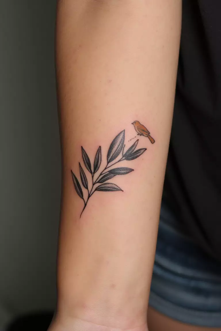 A close up shot of woman's arm with a black ink olive branch and a small bird perched on it tattoo  