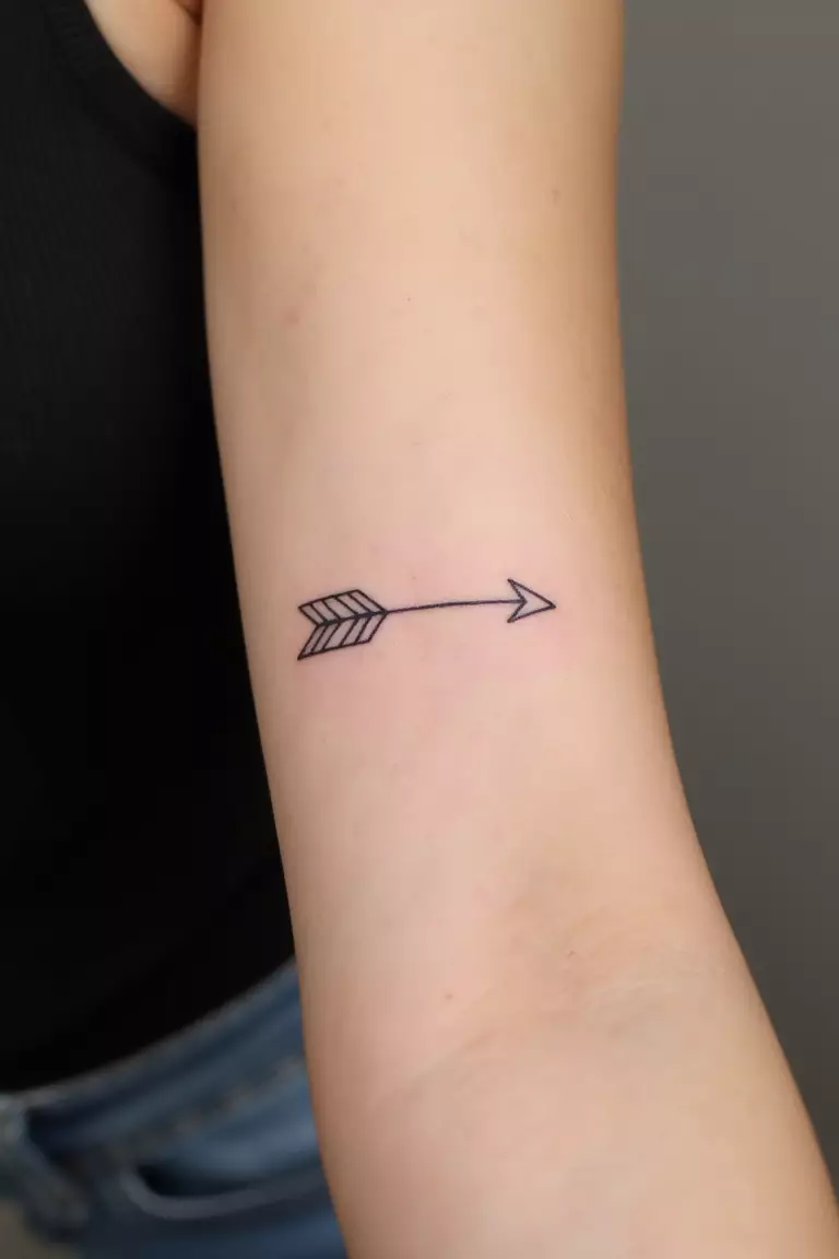 A close up shot of woman's arm with a black ink minimalist arrow outline tattoo, just the basic contours without filling