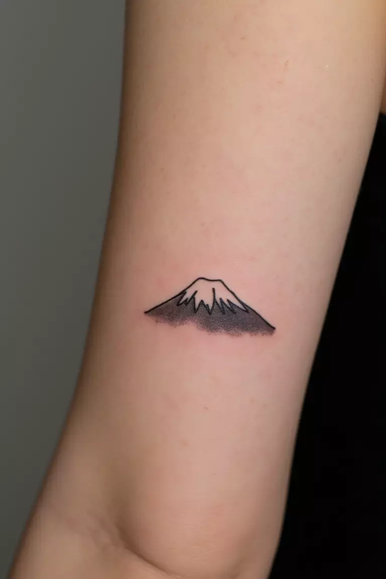A close up shot of woman's arm with a black ink minimalist Mt. Fuji silhouette tattoo  
