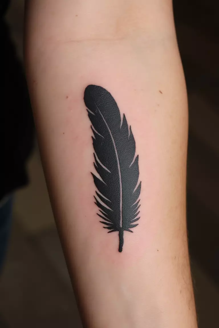 A close up shot of woman's arm with a black ink feather silhouette tattoo, solid black shape with no internal details