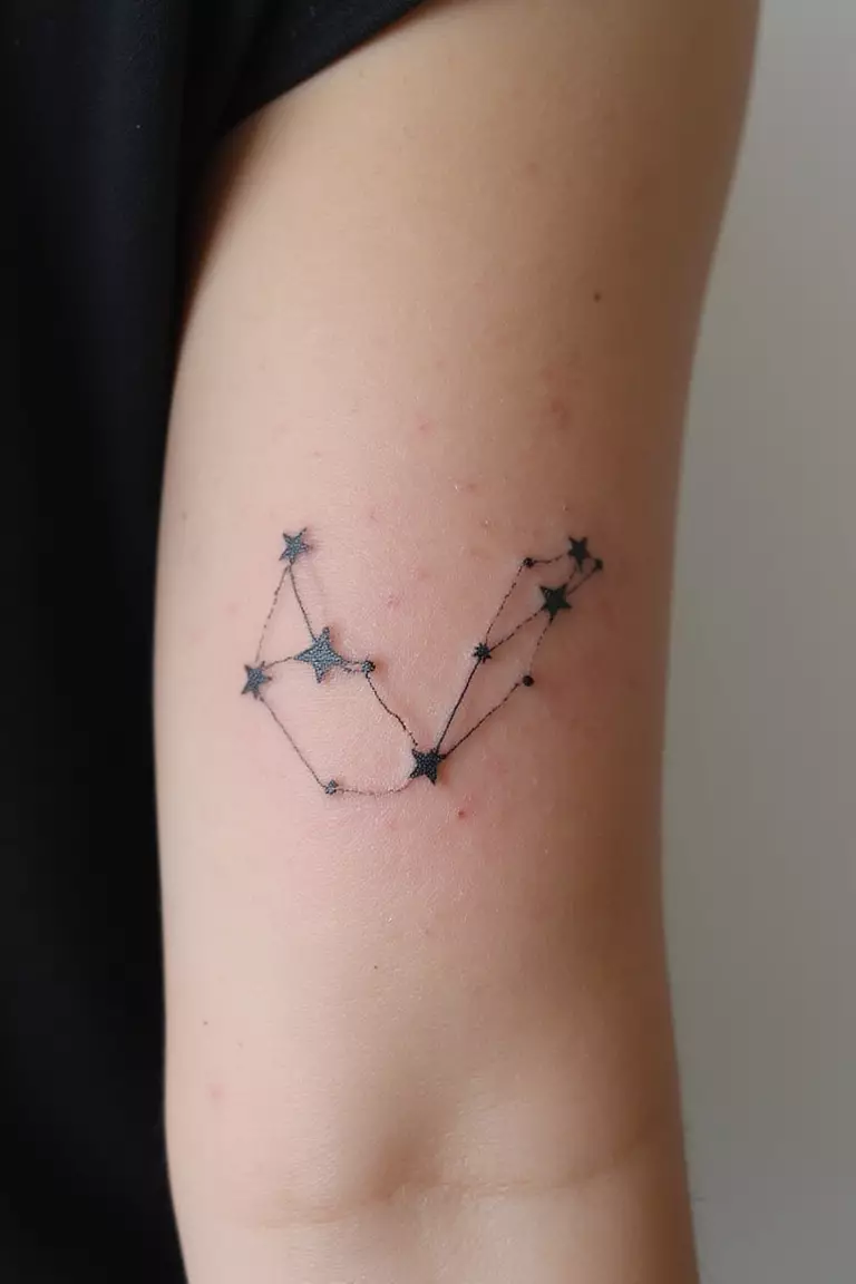 A close-up shot of a woman's arm with a black ink tattoo of the Big Dipper constellation with stars connected by fine lines.