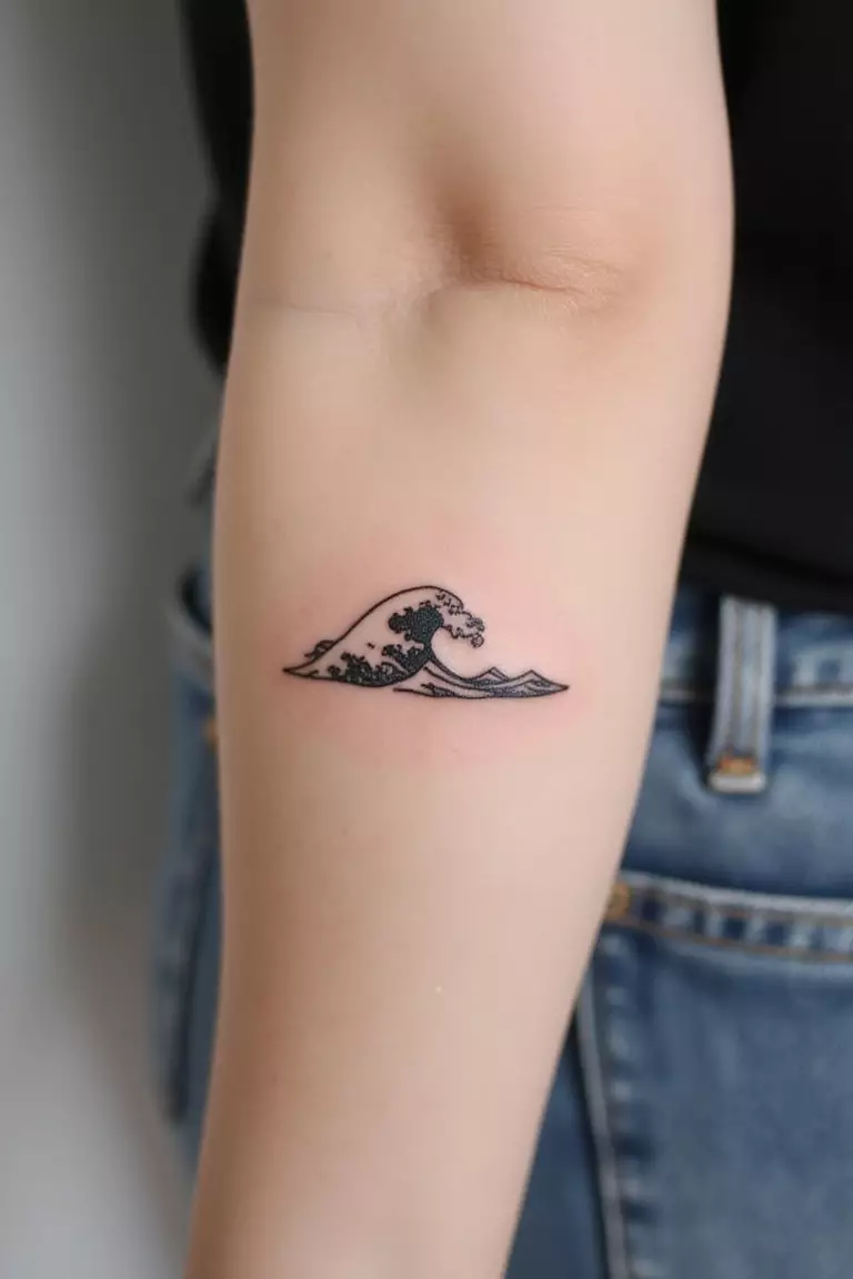 A close-up shot of a woman's arm with a black ink tattoo of a small, simple ocean wave, minimalist lines.