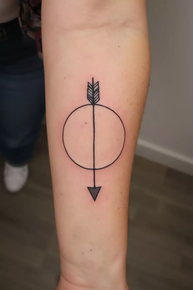 A close up shot of woman's arm with a black ink arrow and circle tattoo, arrow encircled by a perfect circle
