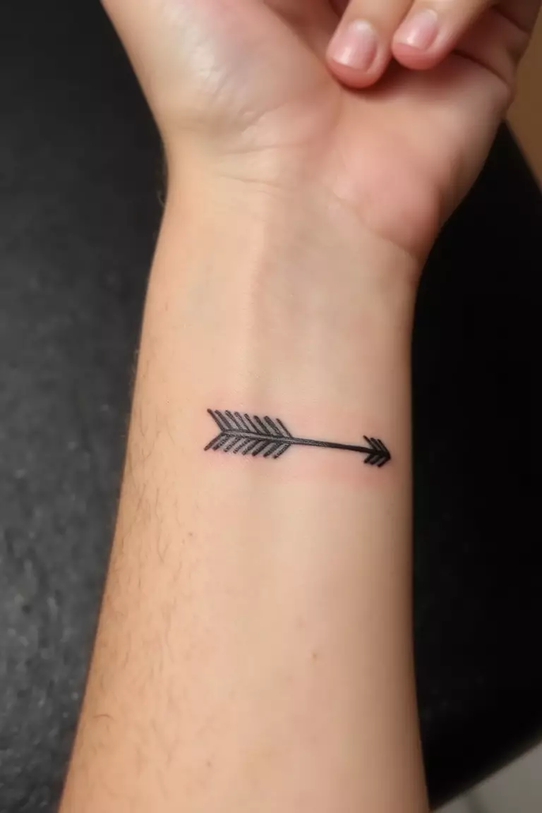A close up shot of woman's arm with a black ink small wrist arrow tattoo, delicate design perfectly positioned on the wrist