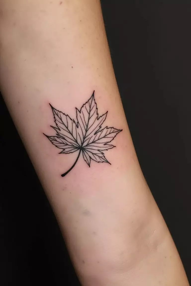 A close up shot of woman's arm with a black ink minimalist Japanese maple leaf design tattoo  