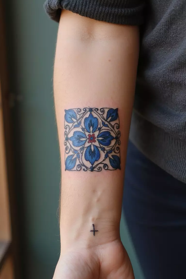 A close-up shot of a woman's arm with a black ink tattoo of a square Talavera tile with intricate blue and white patterns.