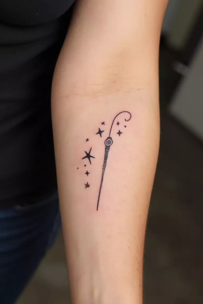 A close up shot of woman's arm with a black ink tattoo of a delicate wand with surrounding stars.